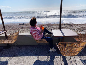 Rear view of woman sitting on chair at beach