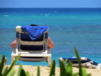Cropped image of person relaxing on deck chair at beach during sunny day