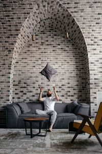 A man with a beard sitting on the sofa and throwing up a pillow