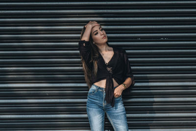 Woman with hand in hair standing by closed shutter