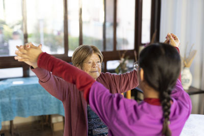 Young nurse holding hands of senior woman to exercise at home