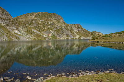 Scenic view of lake and mountains against clear blue sky