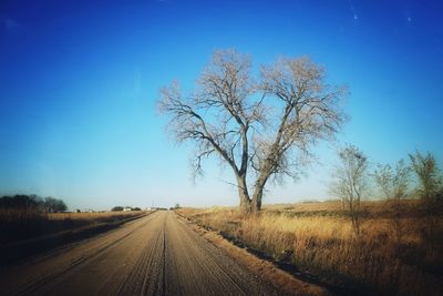 Road passing through field against clear blue sky