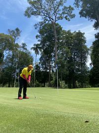 A golfer putting on the putting green with a scenic view of trees against blue sky