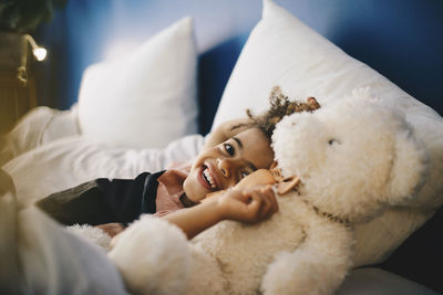 Portrait of happy boy lying with teddy bear on bed at home