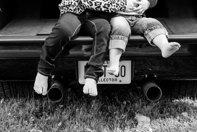 Low section of siblings sitting on vintage car