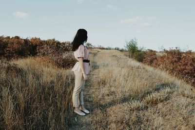 Side view full length of woman standing on grassy field against sky