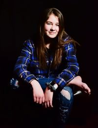 Portrait of smiling teenage girl sitting against black background