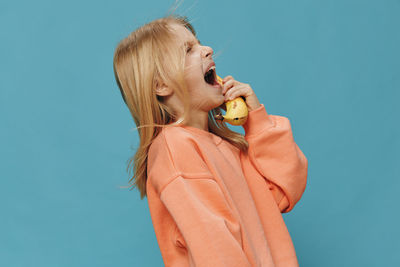 Happy girl holding banana against blue background