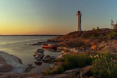 Lighthouse by sea against sky during sunset