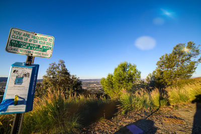 Road sign by trees against blue sky