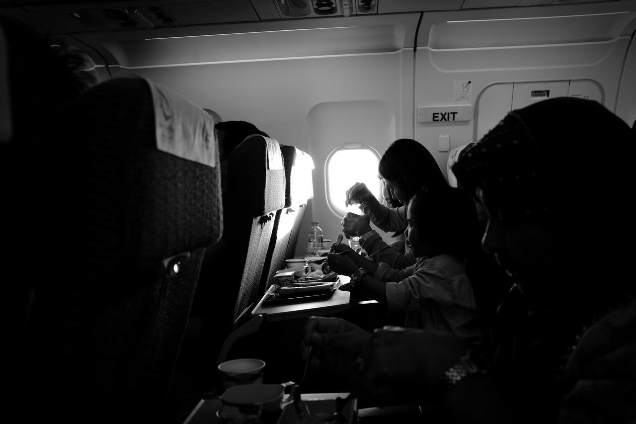 group of people, sitting, men, real people, transportation, women, adult, mode of transportation, vehicle interior, people, travel, indoors, side view, airplane, lifestyles, air vehicle, seat, food and drink