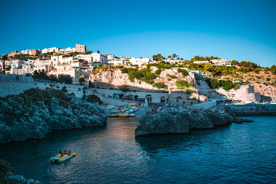 Buildings by sea against clear blue sky