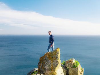 Man standing on rock looking at sea against sky