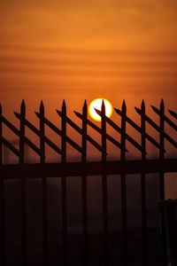 Silhouette railing by sea against sky during sunset