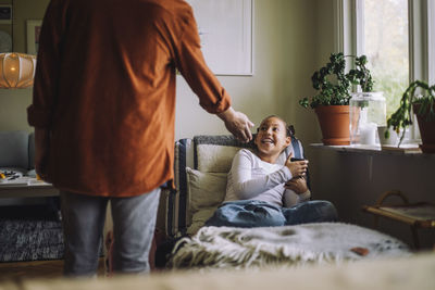 Rear view midsection of father asking smart phone from daughter sitting on bed at home