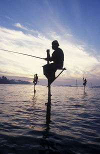 Silhouette fishermen fishing over sea against sky during sunset