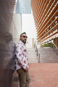 Side view of a bearded male leaning on a office building wall