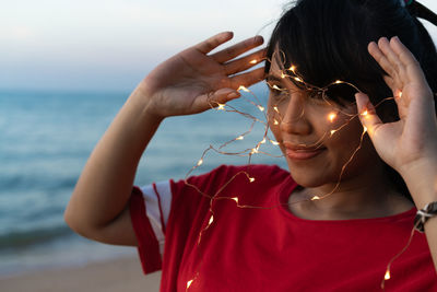 Woman with illuminated string lights looking away at beach