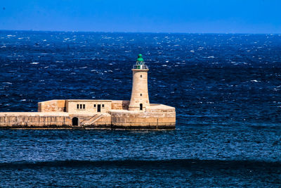 Lighthouse by sea against building and sky