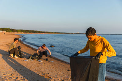 Rear view of man sitting at beach against clear sky