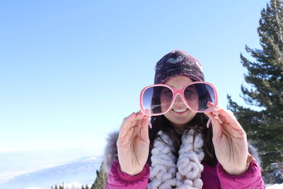 Portrait of young woman holding sunglasses while standing against clear sky