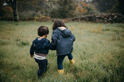 Rear view brother and sister playing in the grass