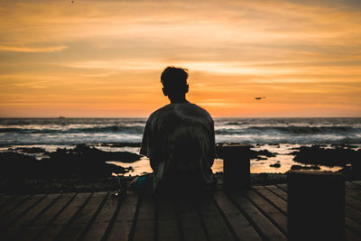 Rear view of a man sitting on shore during sunset