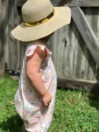 Side view of baby girl wearing hat while standing on grassy field