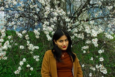 Portrait of beautiful young woman standing by flower tree