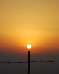 Silhouette barbed wire against orange sky