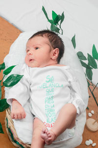 Beautiful newborn baby with eyes open, overhead shot, top view in bamboo fiber basket and surrounded