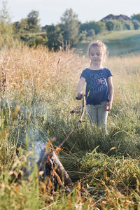 Cute girl holding stick in campfire on grassy field