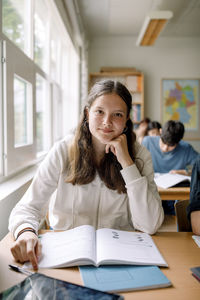 Portrait of teenage girl with book on desk in classroom