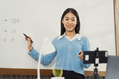 Portrait of a smiling young woman standing against wall