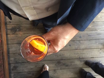 Low section of man holding drink glass on floorboard