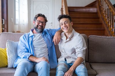 Portrait of smiling father and son sitting on sofa at home