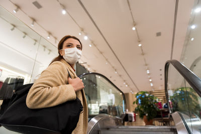 Low angle view of woman wearing mask on escalator