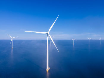 Wind turbines in sea against blue sky