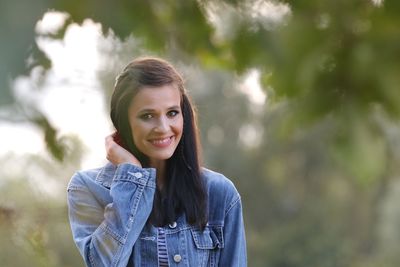 Portrait of smiling young woman against trees