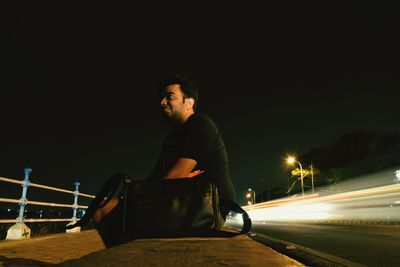 Low angle view of man sitting by road against sky at night