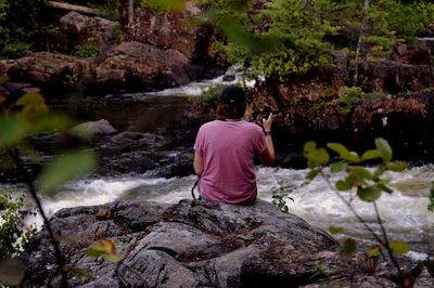 Rear view of man sitting on rock in forest