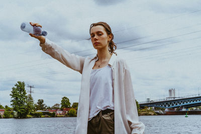 Portrait of confident non-binary person pouring water from bottle against sky