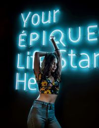 Woman standing by illuminated text at night