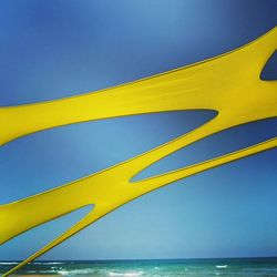Close-up of yellow umbrella by sea against clear sky