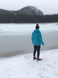 Rear view of teenage girl standing on snow covered mountain lake