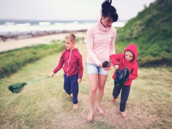 Full length of mother with sons on grassy field at beach