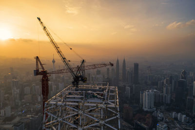 Cranes at construction site against sky during sunset