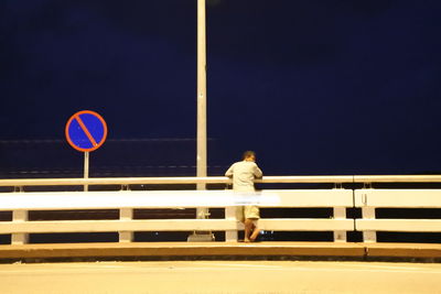 Man standing by railing against sky at night