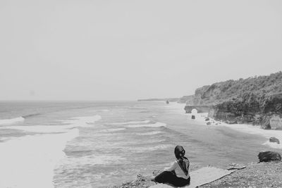 Man sitting on beach against clear sky